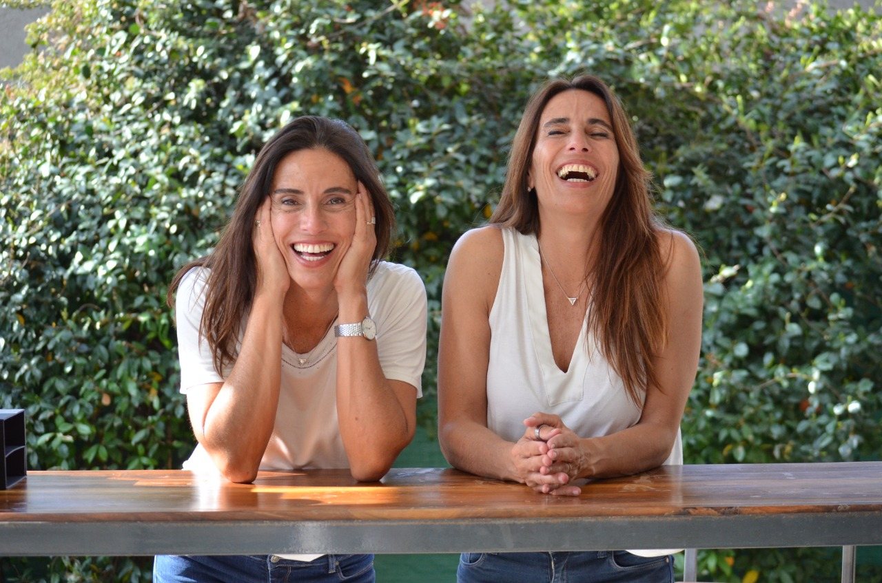 Flor y Celi, fundadoras de TwinPack, riéndose en una mesa de trabajo