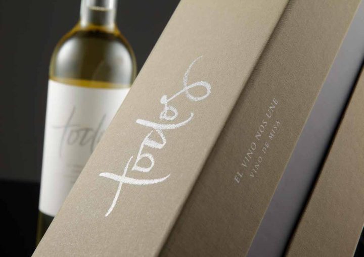 Estuche kraft con caligrafía blanca junto a una botella de vino blanco